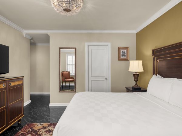 A bedroom with a bed, TV, and dresser. There's a lamp on the side table, a mirror with a chair reflection, and a ceiling light.