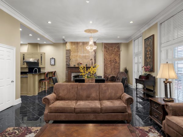A spacious living room with beige walls, brown sofas, a chandelier, bar area, and decorative elements like art pieces and plants.
