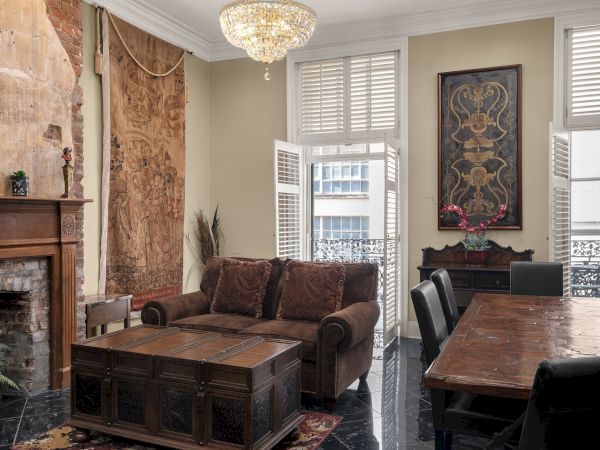 A cozy living room with a fireplace, chandelier, tapestry, couch, coffee table, dining table, and art on walls.