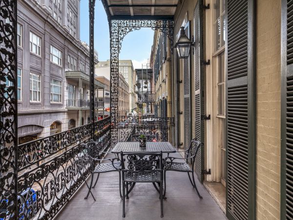 A wrought iron balcony with a table and chairs, overlooking a street with classic buildings and intricate architectural details.