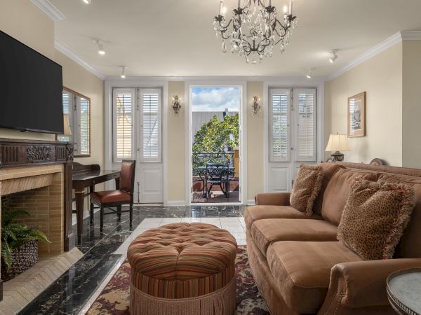 A cozy living room with a chandelier, sofa, cushions, ottoman, fireplace, TV, and a view of an outdoor patio with furniture through glass doors.